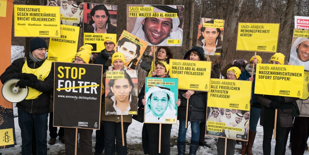 A group of people holding signs calling for Saudi Arabia to free peaceful activists from jail