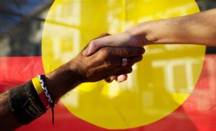 Indigenous and Non-Indigenous Australians shaking hands in front of the Aboriginal flag