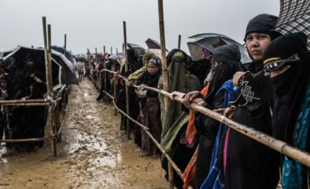 Rohingya lining up by a fence in the mud