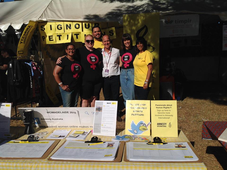 Amnesty's women's rights activists stand in front of a stall at WOMAD