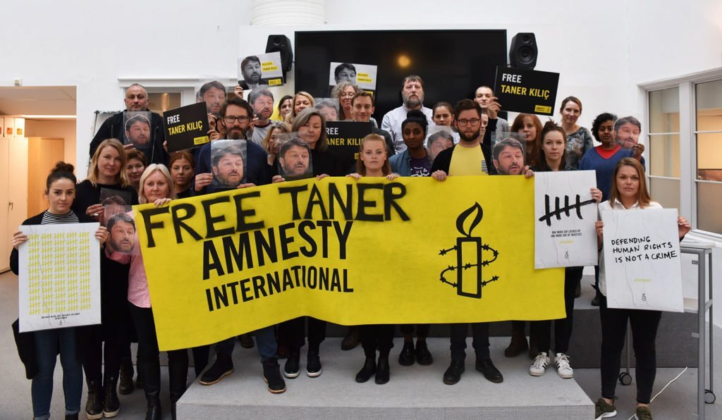 A group of Amnesty Norway staff stand holding posters that say 'Free Taner'