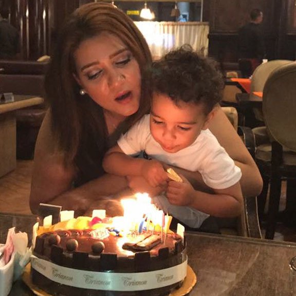 A mother (Amal Fathy) holding her child at a restaurant. They are blowing out candles on a birthday cake.