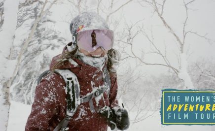 Woman in ski attire smiles under falling snow