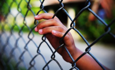 Young child's hand behind a fence.