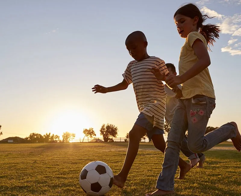 Children racing after a football playing on a field.