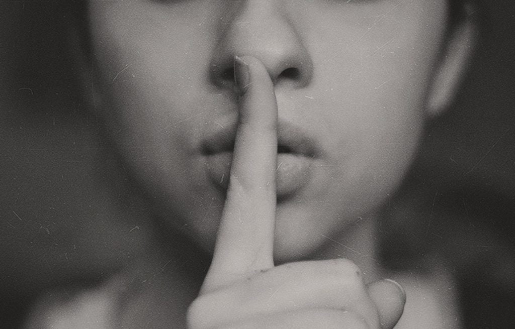 Close up photo of the lower half of a woman's face. She is holding her finger in front of her mouth.