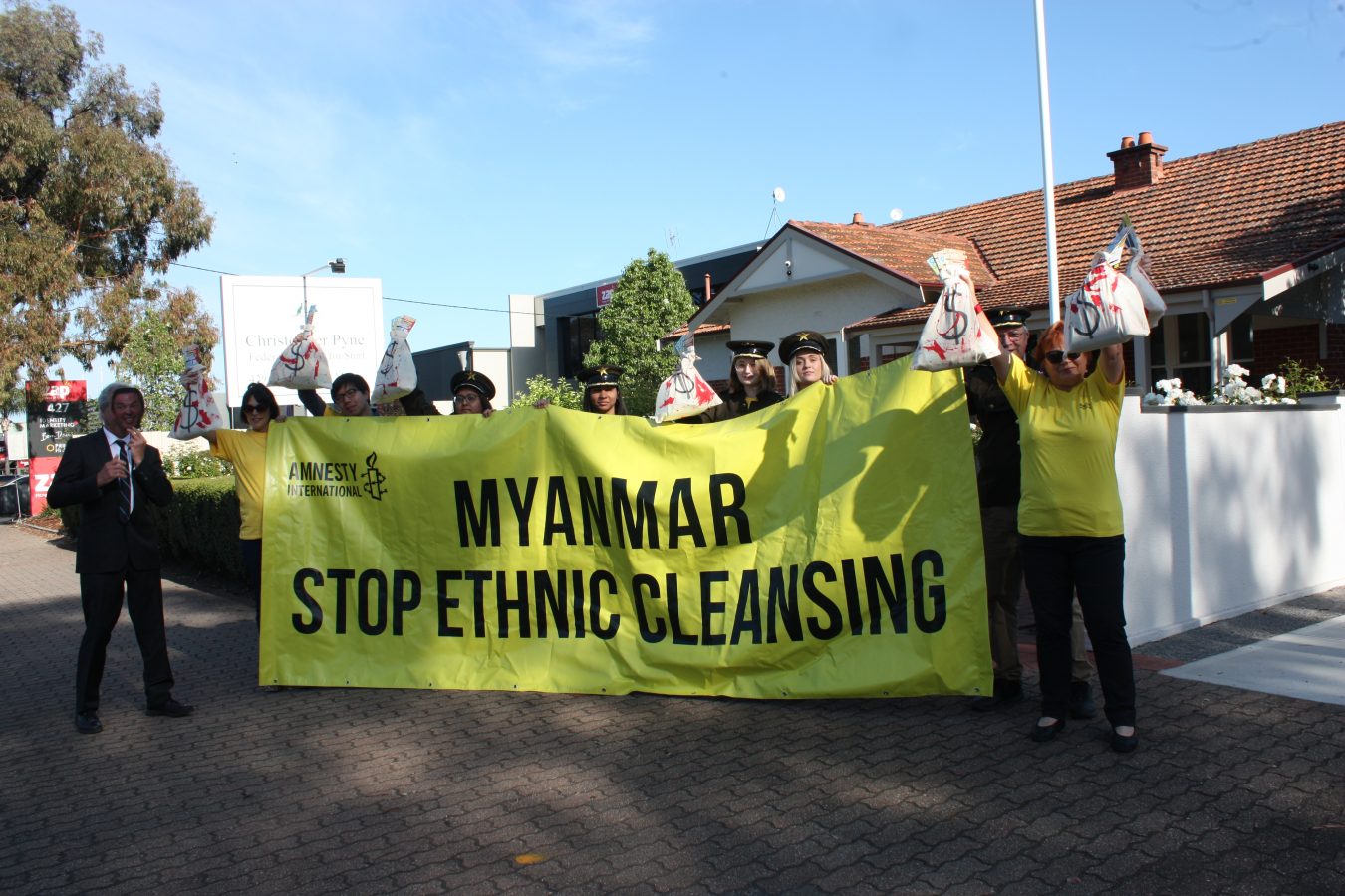 a group of people standing on a footpath with a large yellow sign saying 'Myanmar stop ethnic cleansing'