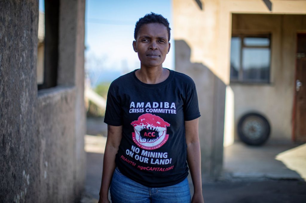 A woman with cropped hair wearing a black tshirt with writing on it: Amadiba crisis committee no mining on our land!