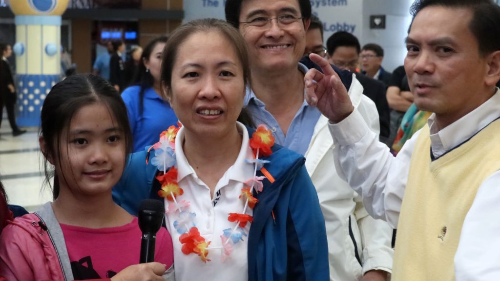a woman with family and friends around her at an airport arrivals hall.