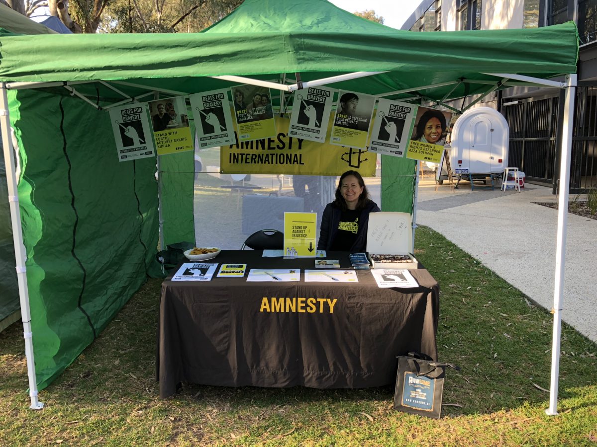 Volunteer sitting at Amnesty marquee stall covered in Amnesty promotional material
