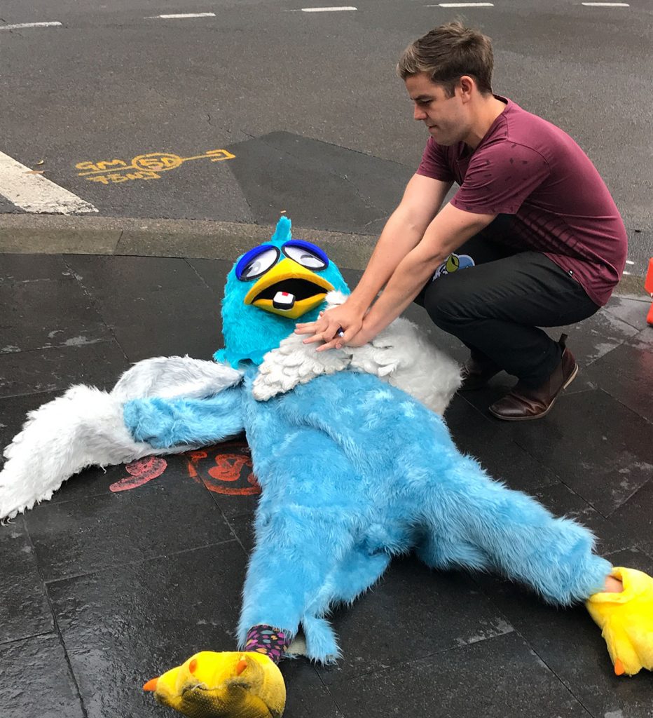 A man pretends to resuscitate a person dressed up in a Twitter bird costume. 
