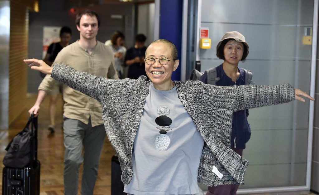 A woman with a big smile on her face and her arms stretched wide to hug someone off camera. She is in an airport.