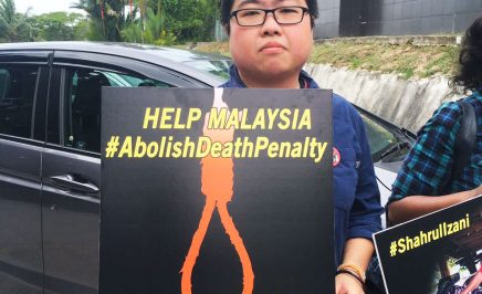 A Malaysian man holds a sign towards the camera. The sign reads: 'Help Malaysia #AbolishDeathPenalty