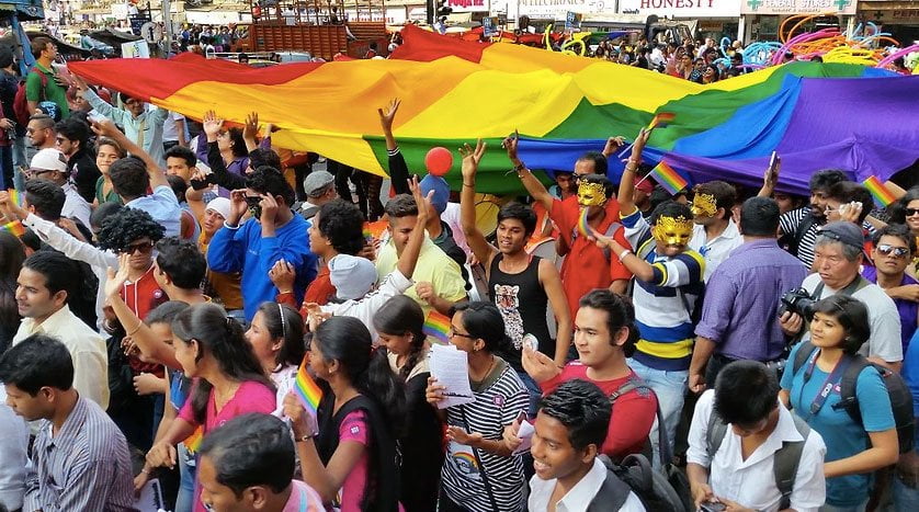 A group of people smiling and waving their arms and rainbow flags.