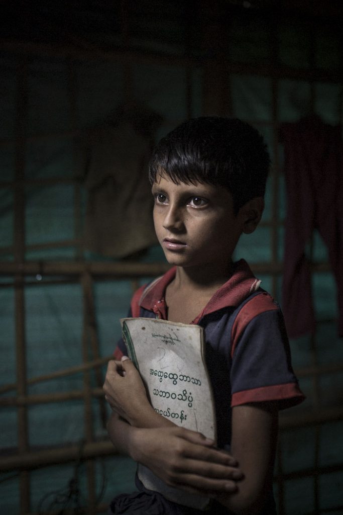 A young Rohingya boy holds a school book in a refugee camp in Bangladesh.