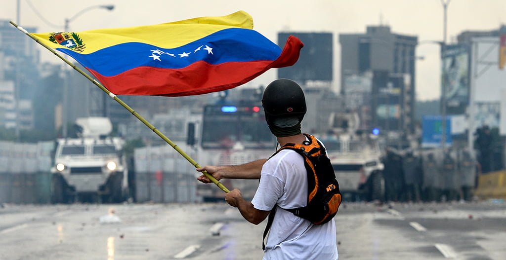 A Venezuelan opposition demonstrator waves a flag at the riot police in a clash during a protest against President Nicolas Maduro, in Caracas in 2017