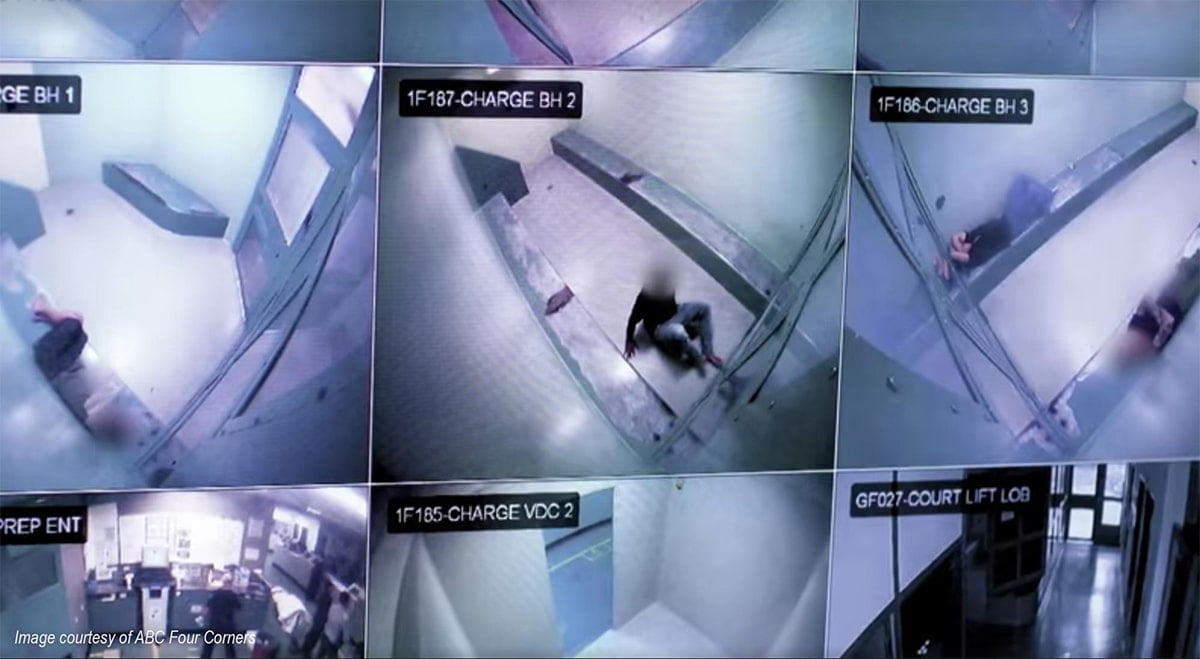 9 camera feeds on the one computer screen, showing blue-hued images looking down at bare cells. A blurred figure is curled on the floor of one cell image.