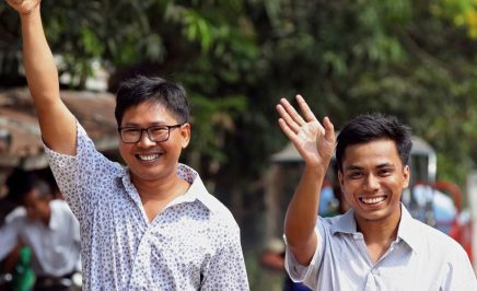 Wa Lone and Kyaw Soe Oo smile widely and wave. Wa Lone has his hand raised in the air in a thumbs up.