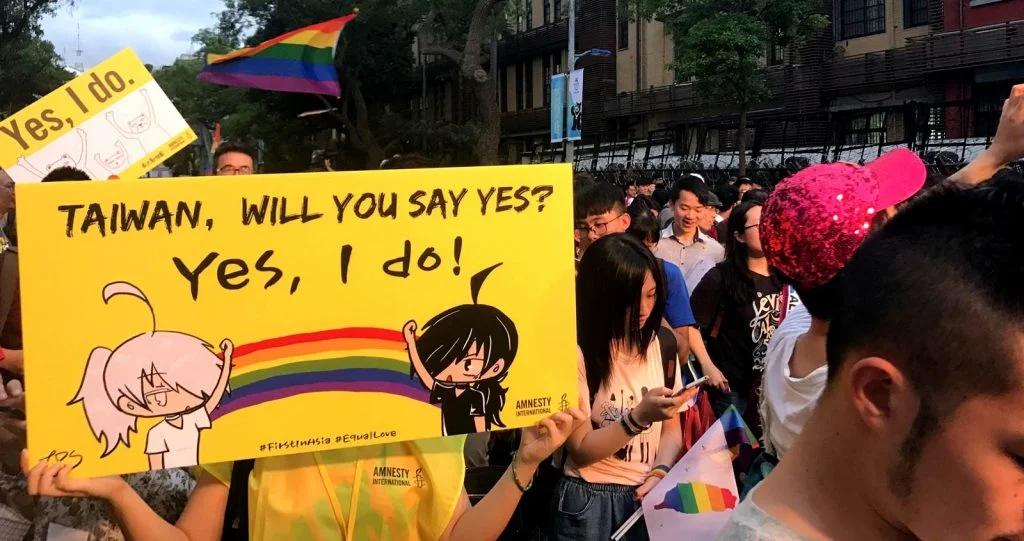 Crowd of people with rainbow flags. One person holding a yellow sign with a rainbow and words: Taiwan, will you say yes? Yes, I do!