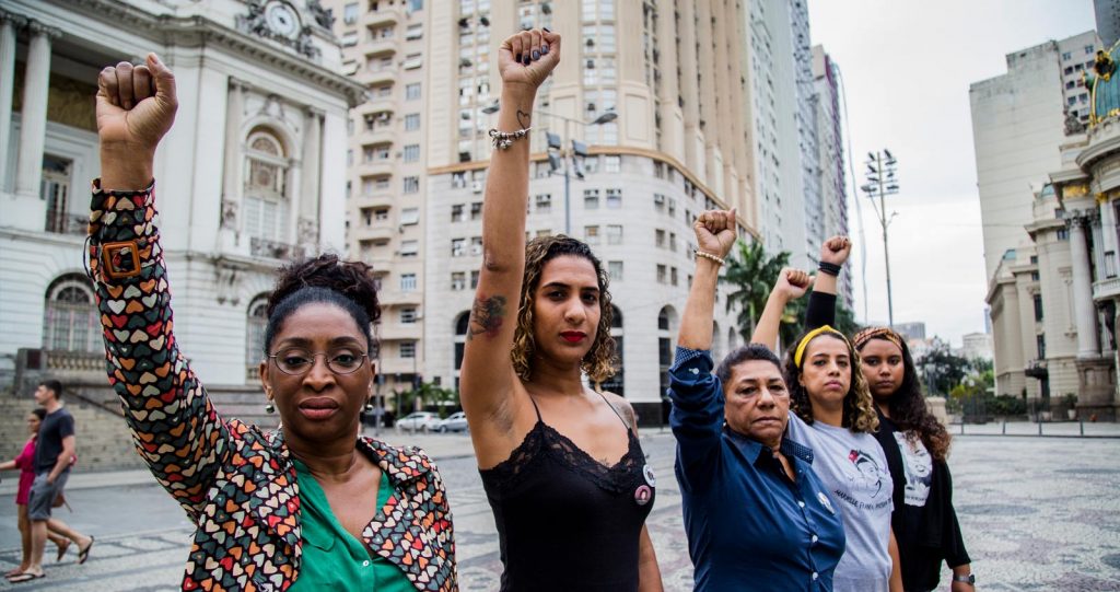 A public square, where a row of five women hold a clenched hand up in the air, in an act of solidarity.