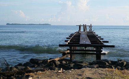An old wooden jetty over a clear ocean water and with a sandy beach