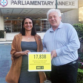 A man and a woman hold a yellox box with a sign on it reading: 17,838 people signed to get kids out of watch houses