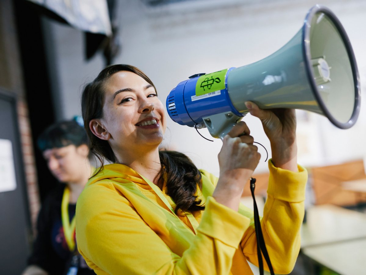 A young woman wearing a yellow hoodie and holding a loudspeaker