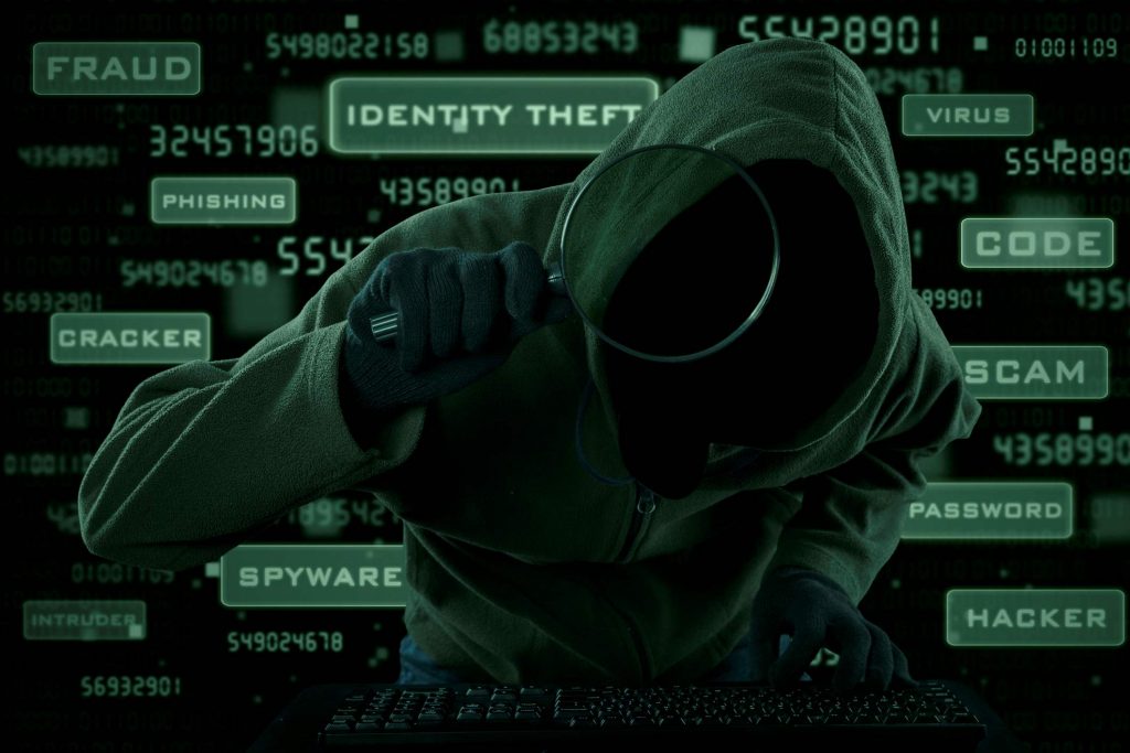 An ominous, hooded body holds a magnifying glass. Words such as 'identity theft', 'spyware' and 'code' are in the background.