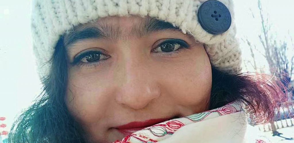 A young woman wearing a white knitted beanie and a white floral patterned scarf.