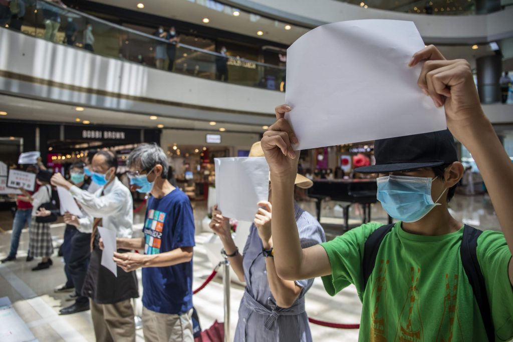 A group of people wearing face masks hold protest signs in a busy shopping mall in Hong Kong.