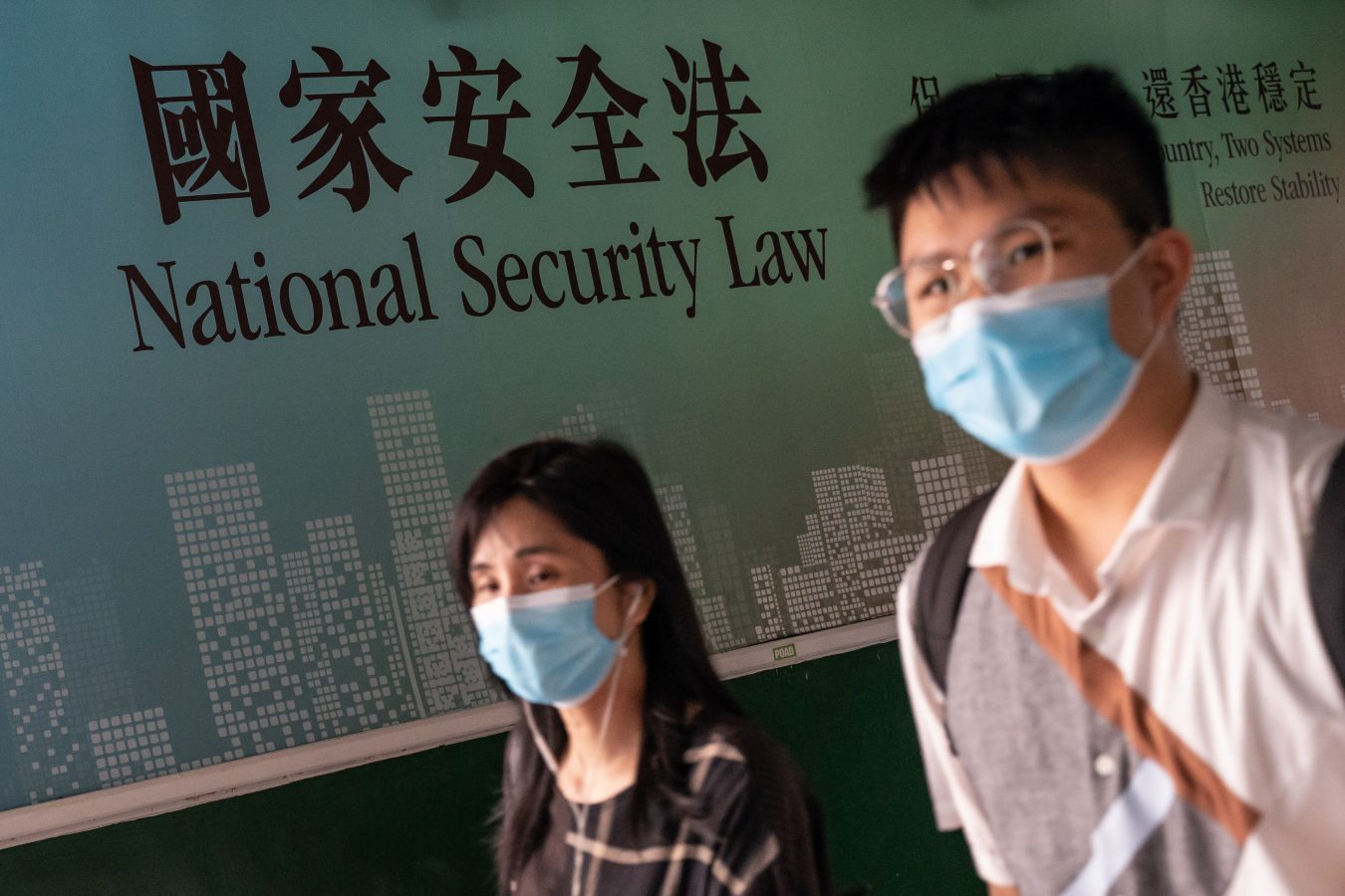 Two people wearing masks walk past a sign that reads 