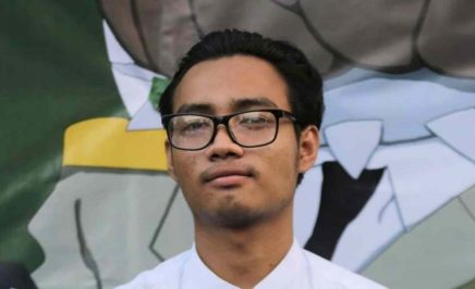 Paing wears a white shirt and dark glasses in front of a green mural.