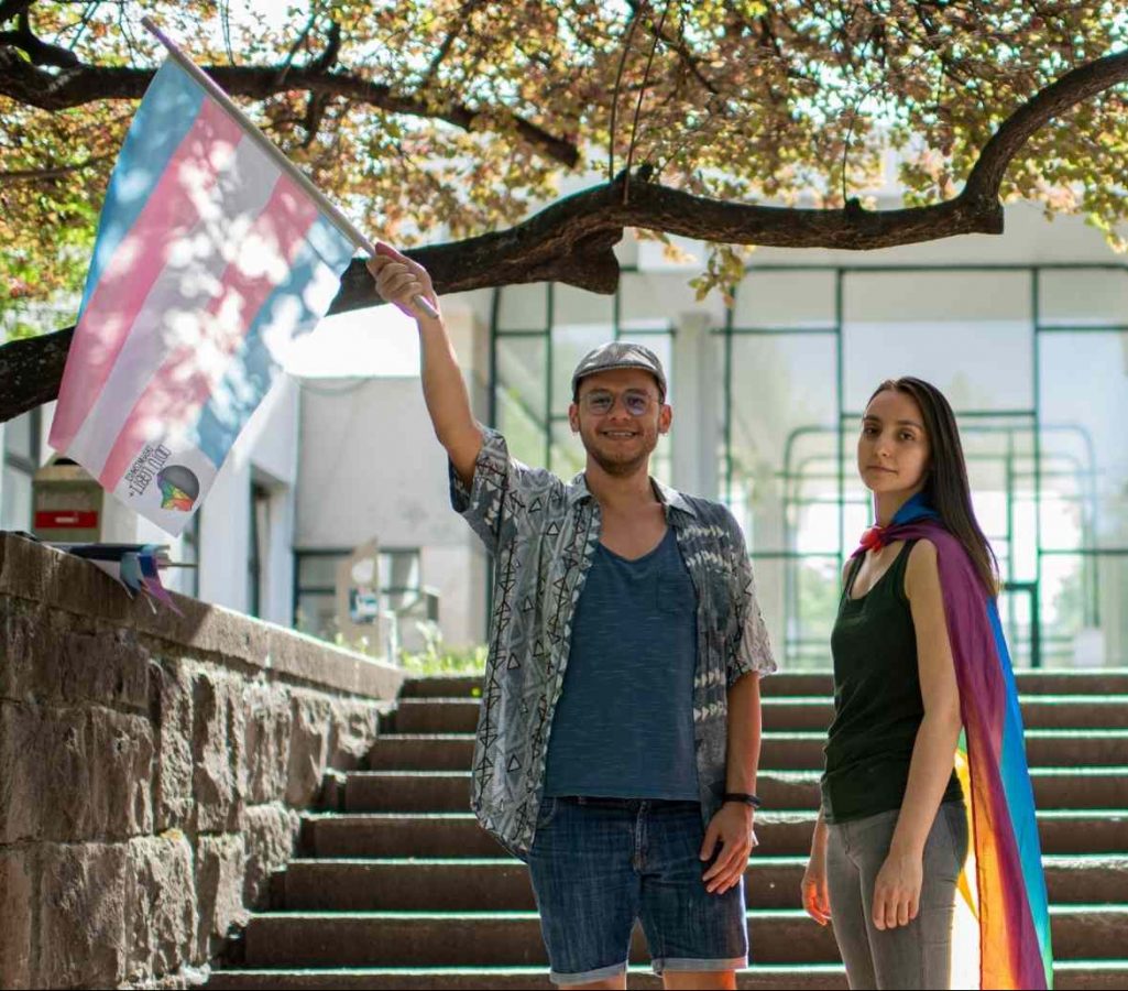 Melike and Ozgur wave a rainbow flag in front of grey steps.