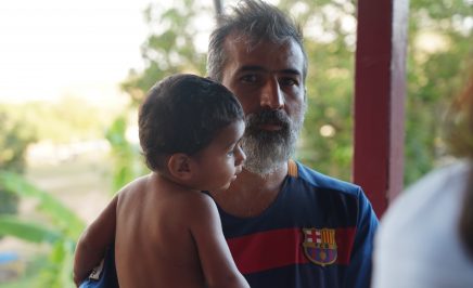 Papi in a Barcelona jersey and a grey beard sits with his son Cyrus on his lap before some trees.
