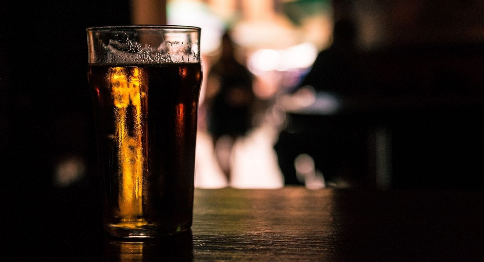 A pint of beer sitting on a wooden bench in a dark-lit room