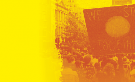 Sign reading 'We Stand Together' on Aboriginal Flag at a rally