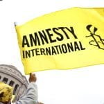 Image of a yellow and black flag, featuring the Amnesty International logo, being waved.