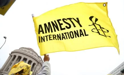Image of a yellow and black flag, featuring the Amnesty International logo, being waved.