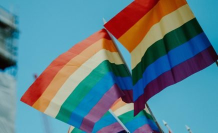 LGBTQIA+ flags waving against a blue sky
