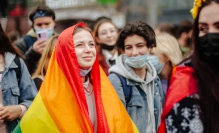 Wide shot of a group of women activists in Kyiv Pride march in 2021. One woman has a rainbow flag draped on her person.