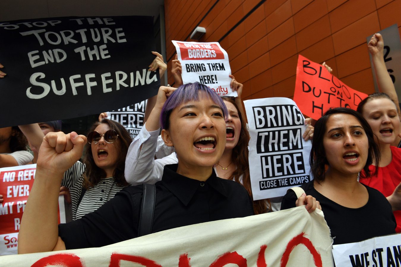 Refugee advocates shout slogans as they protest at the Immigration and Department of Foreign Affairs and Trade building in Sydney. Signs read 'Bring them here' and 'Open the borders'.