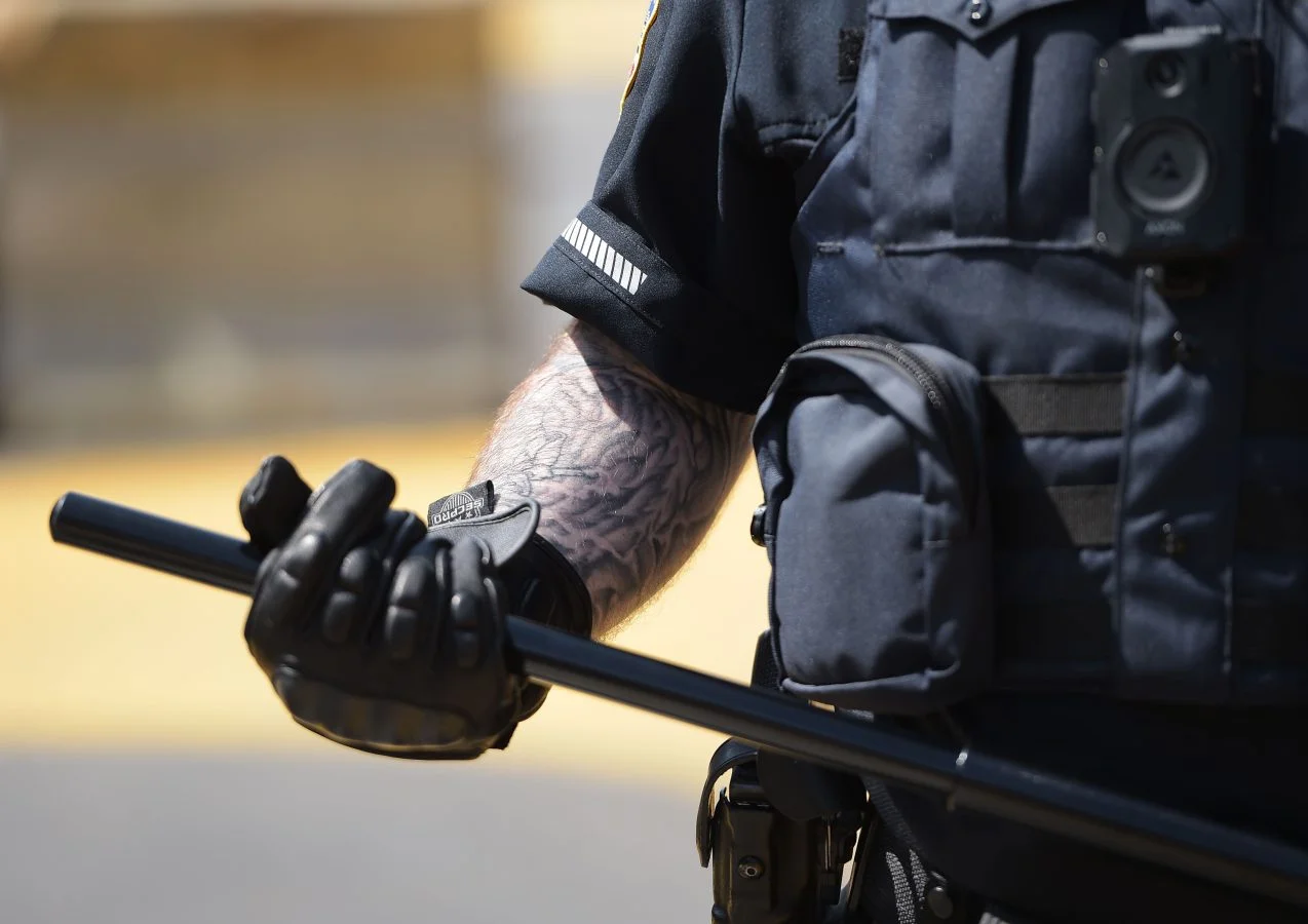 Police officer in dark blue riot gear holds a black baton