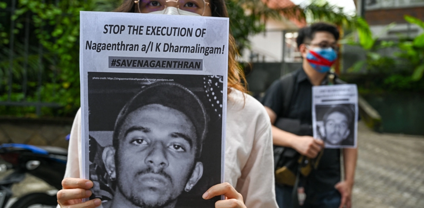 Human rights protestor holds sign to camera which reads 'Stop the execution of Nagaenthran K Dharmalingam #SaveNagaenthran