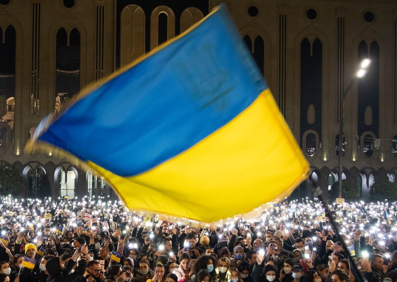 People gather for a rally in support of Ukraine in front of parliament, Ukraine flag waving in the wind is front and centre.
