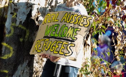 An activist at the 2022 Palm Sunday Walk for Justice for Refugees in Naarm holding a sign saying 