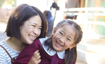 Mother holds daughter in school uniform, as both smile