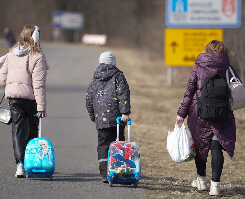 Three young children walking down a road with suitcases.