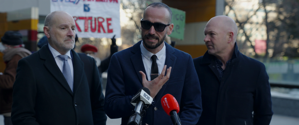 Moz wearing sunglasses, standing out the front of the federal court. to his left is Michael Bradely from marque lawyers, and to his right is Tim Oconner from Amnesty International