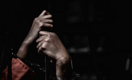 An artistic shot of a prisoner's hands holding prison cell bars.