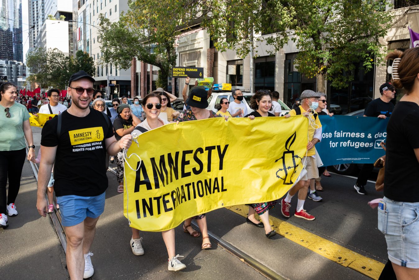 A group of people at a march holding a black and yellow Amnesty International banner between them